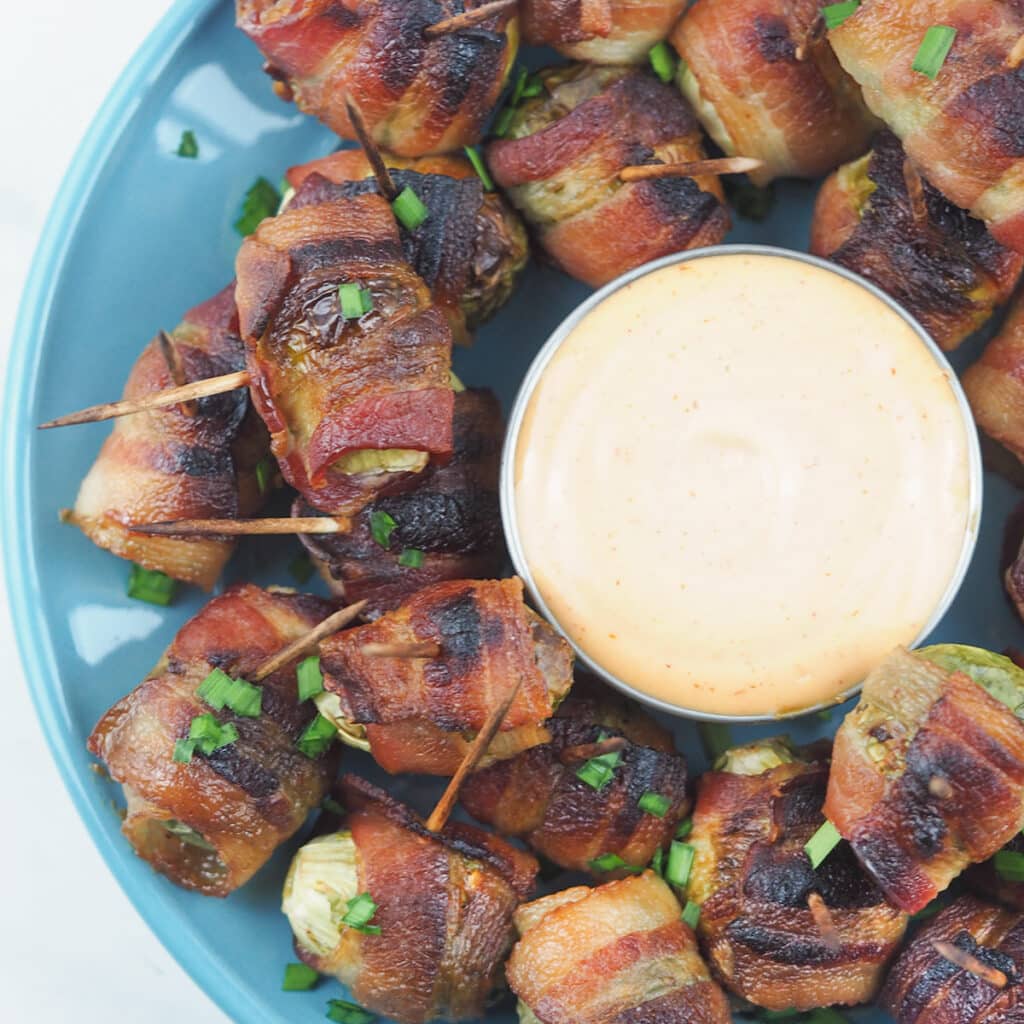 top view of bacon brussel sprouts on blue serving plate with dipping sauce