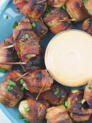 top view of bacon brussel sprouts on blue serving plate with dipping sauce