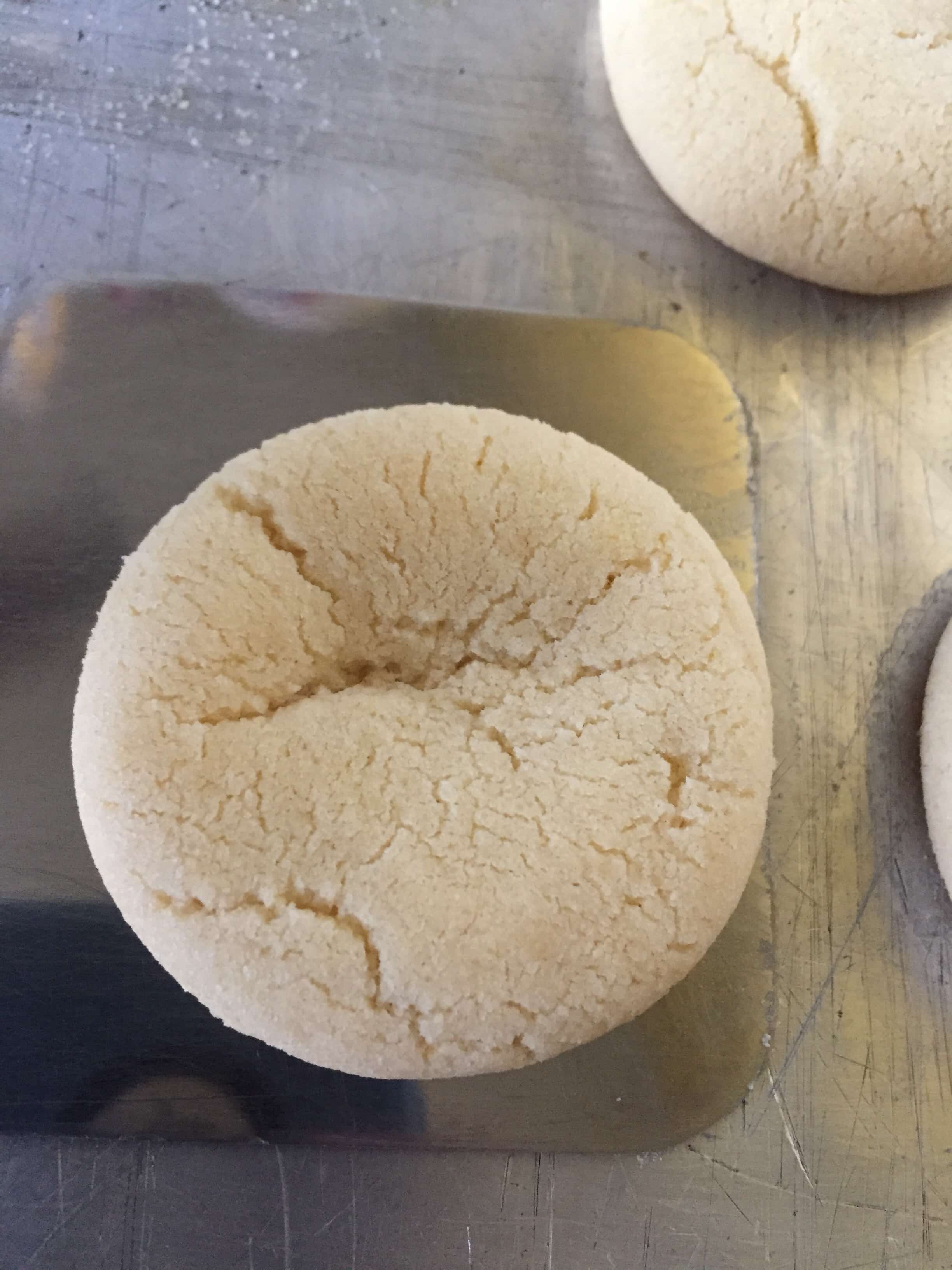 Baked sugar cookies being lifted off a metal baking sheet with a metal spatula