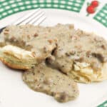 close up of biscuits and gravy on white plate with green plaid rim with fruit detail