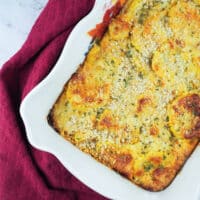 baked summer squash casserole in dish with a ribbon edge surrounded by a purple towel