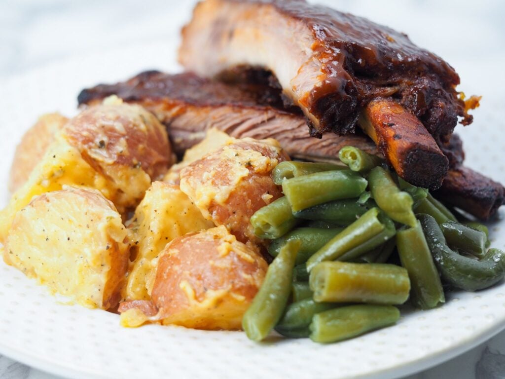 cheesy potatoes with ribs and green beans on white plate