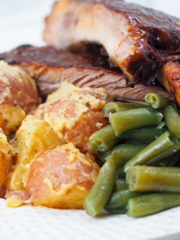 cheesy potatoes with ribs and green beans on white plate