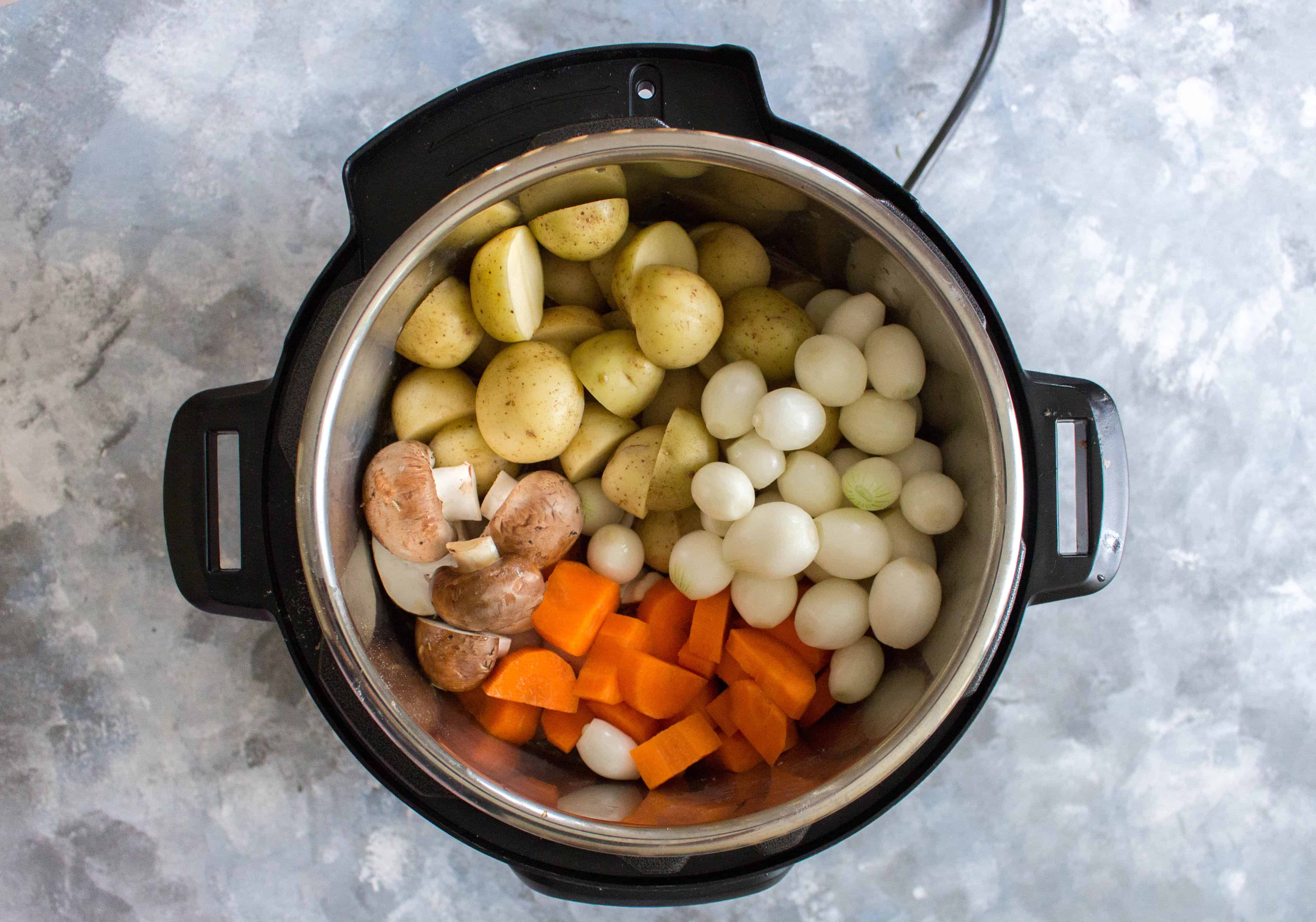 instant pot on table filled with potatoes, pearl onions, carrots, and mushrooms