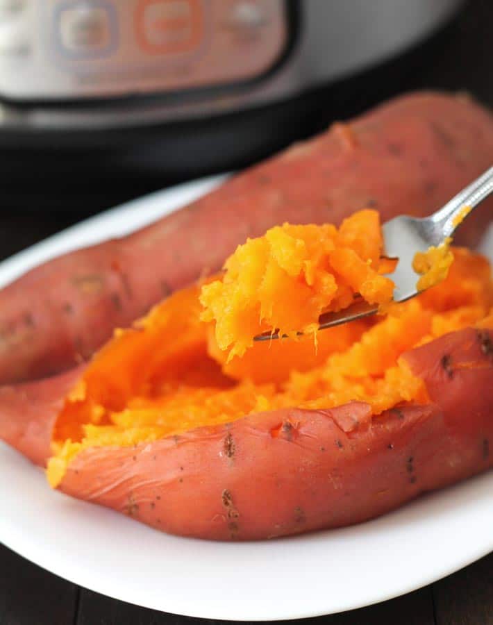Cooked sweet potato on a white place with an Instant Pot in the Background with a bite of sweet potato on a suspended fork