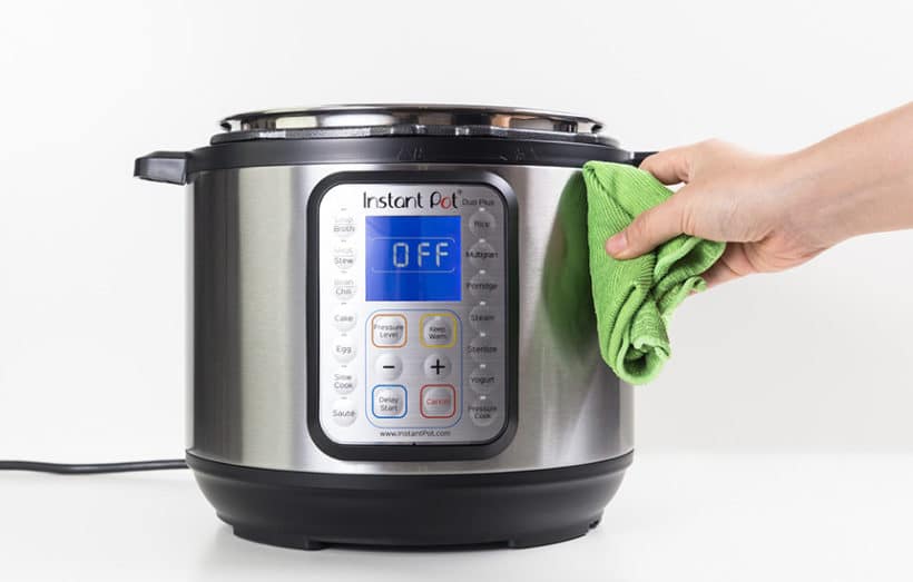 pressure cooker being cleaned with a green cloth on a white background