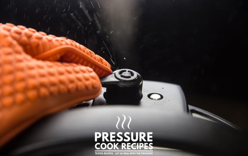 close-up of an instant pot releasing pressure with steam being turned with an orange silicone glvoe