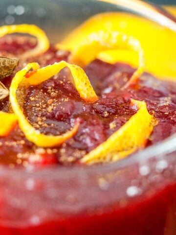 cranberry sauce in a serving dish topped with orange peel and anise with naval orange in backround