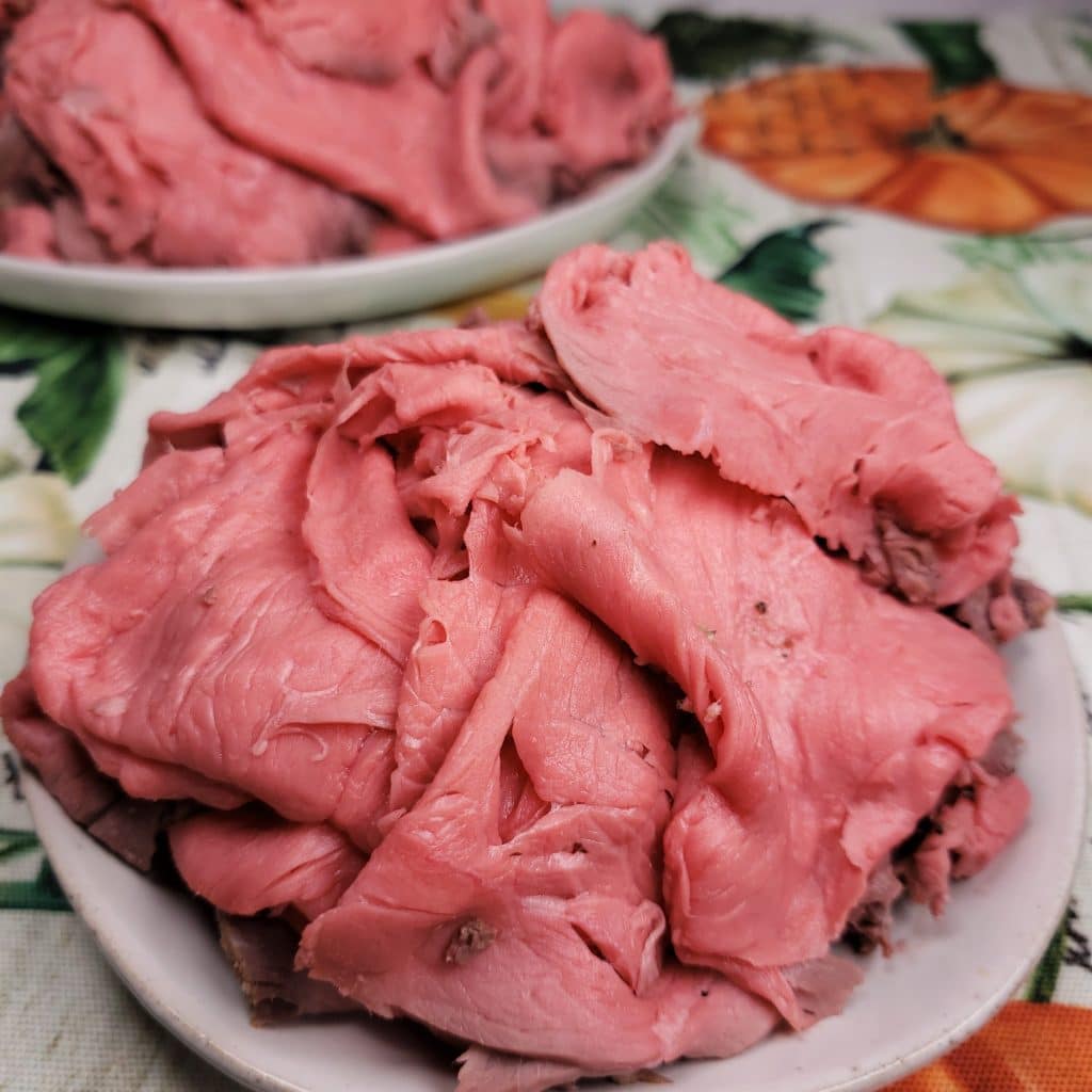 thinly sliced roast beef on a plate set on a table with a floral tablecloth