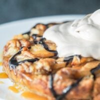 apple galette with cinnamon roll pie pastry on a white plate drizzled with caramel and chocolate syrup topped with chocolate whipped topping