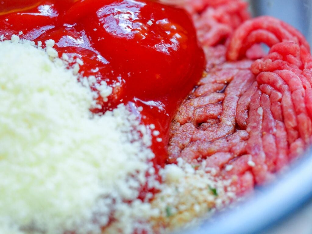 ground beef with ketchup parmesan cheese with spices for a meatloaf mixture in a bowl