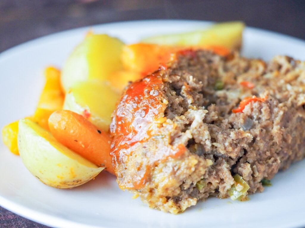 sliced meatloaf on a white plate with roasted potatoes and carrots