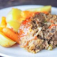 sliced meatloaf on a white plate with roasted potatoes and carrots