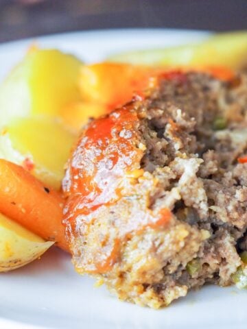 sliced meatloaf on a white plate with roasted potatoes and carrots