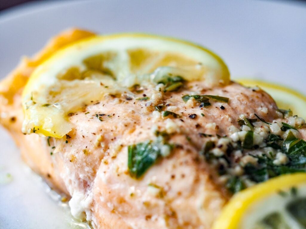 close up of herbed lemon salmon on a white plate with lemon slices