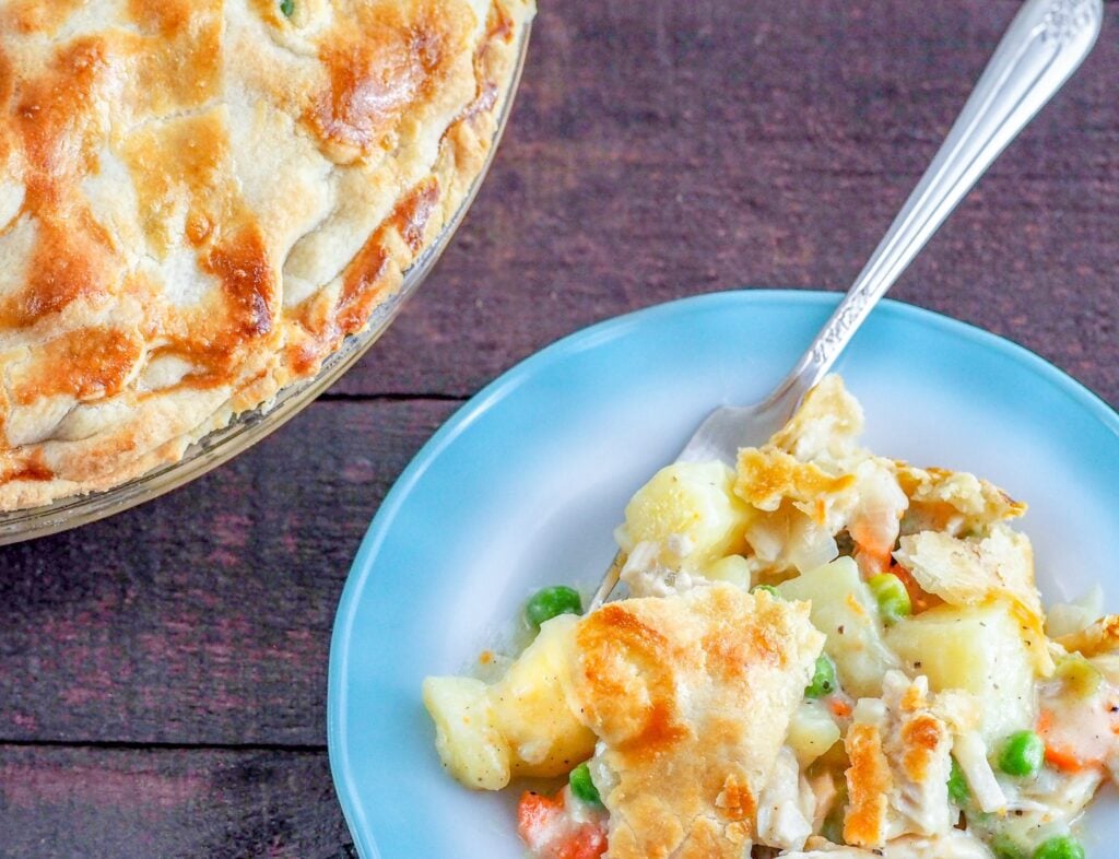 baked chicken pot pie in upper left corner and piece of chicken pot pie on blue-edged ribbon milk glass plate with antique fork