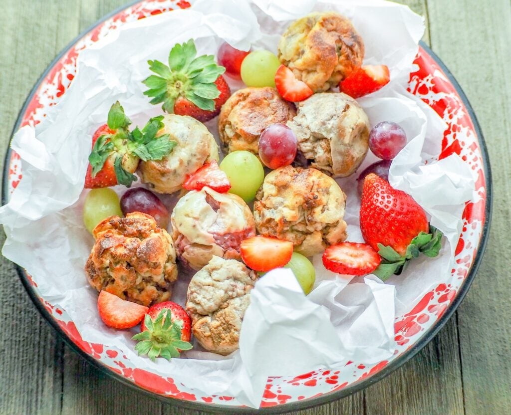 french toast bites on a red and white metal pie plate with crumpled parchment paper with grapes and strawberries