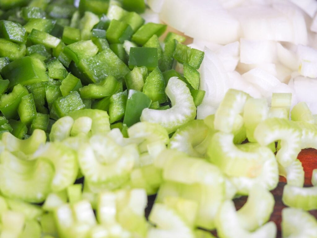diced green peppers and onions with sliced celery on a wooden cutting board
