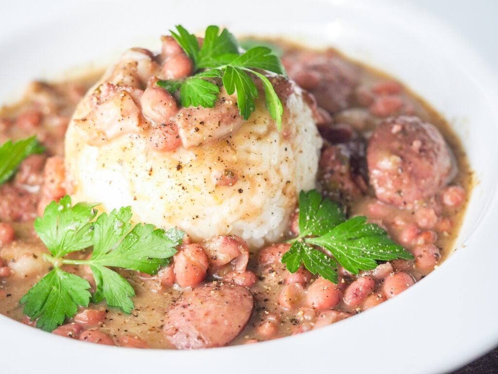 red beans and rice with sausage in a large white bowl with a formed cup of rice in the middle with fresh pepper and parsley garnish