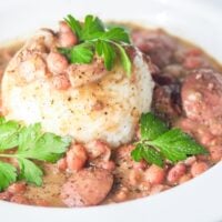 red beans and rice with sausage in a large white bowl with a formed cup of rice in the middle with fresh pepper and parsley garnish