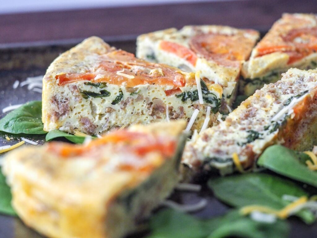 sliced frittata pieces on a bed of spinach lying on a baking sheet