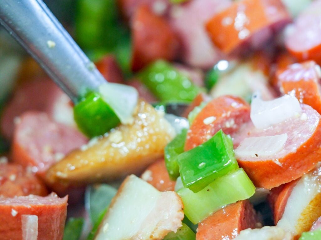 cooked sausage with green peppers, onions, and celery in pan