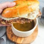 french dip sandwich being dipped into au jus gravy
