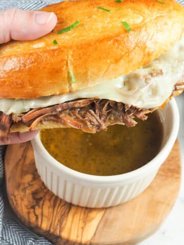 french dip sandwich being dipped into au jus gravy
