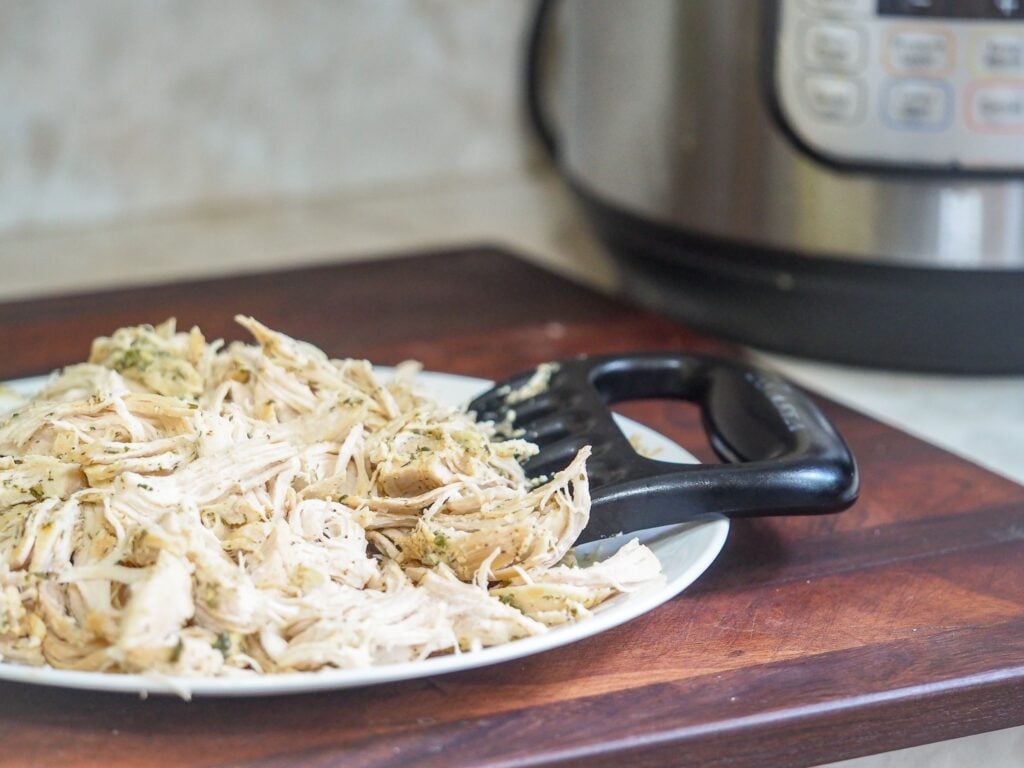 shredded cooked chicken on plate with shredding claw with instant pot in right background