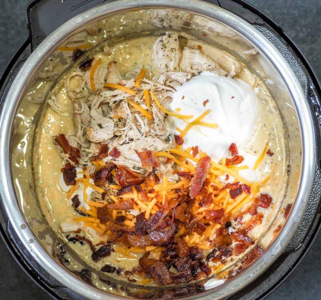 overhead shot of instant pot with cooked chicken cheese crumbled bacon mayo and sour cream