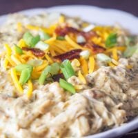 close up of instant pot crack chicken on white platter topped with sliced green onions shredded cheese and crumbled bacon