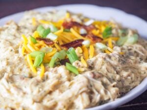 close up of instant pot crack chicken on white platter topped with sliced green onions shredded cheese and crumbled bacon