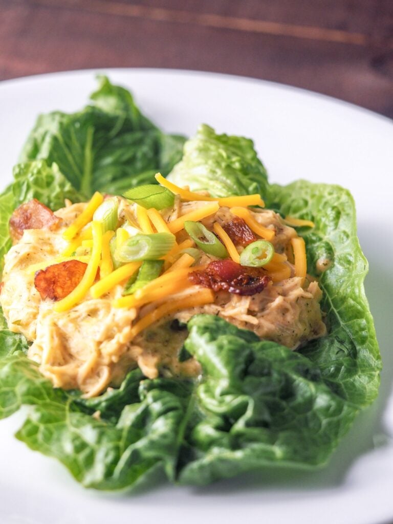 crack chicken served on romaine lettuce on white plate topped with bacon green onions and cheese