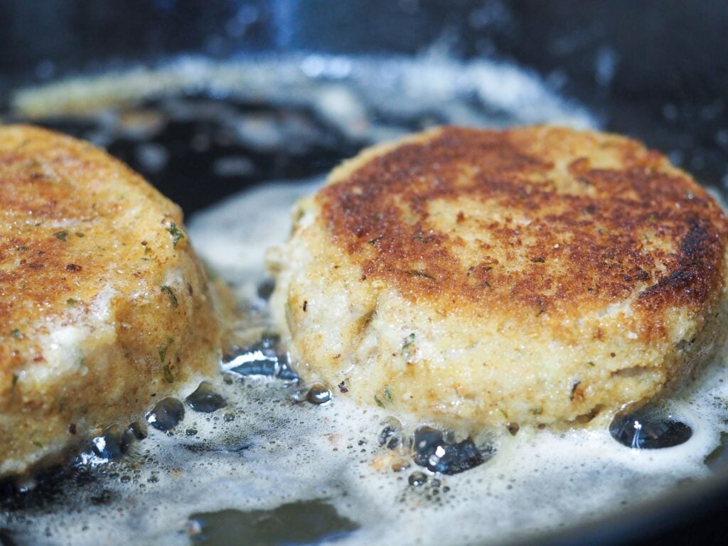 close view of salmon patties being fried in a cast iron pan