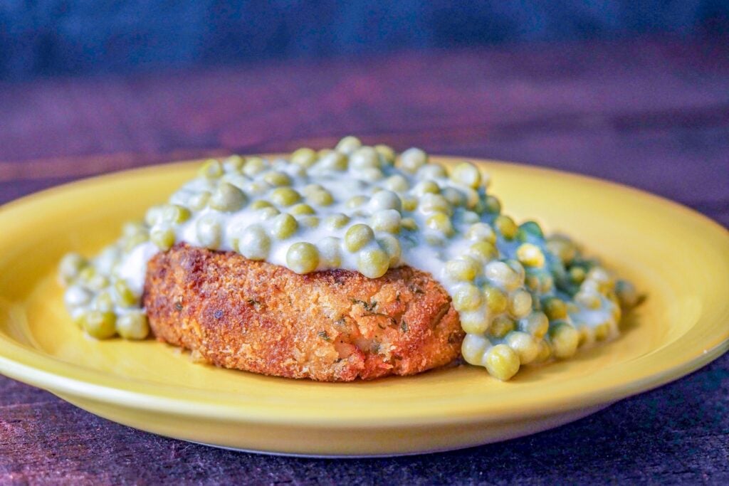 salmon patty on a yellow plate topped with creamed peas