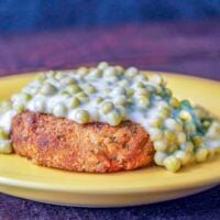 salmon patty on a yellow plate topped with creamed peas