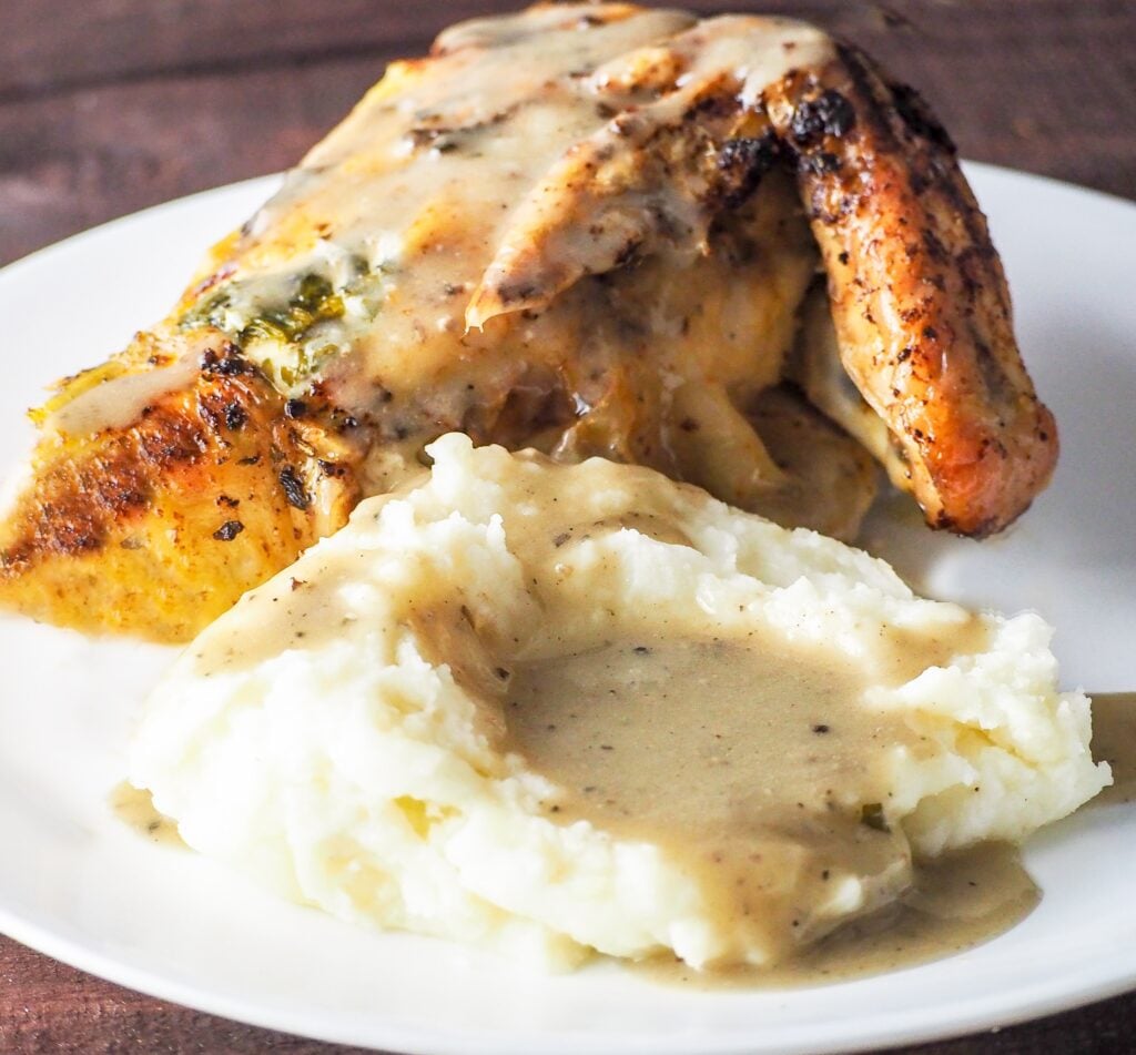 roasted chicken breast with wing attached on a white plate with mashed potatoes and poultry gravy