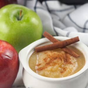 applesauce in white bowl next to red and green apples