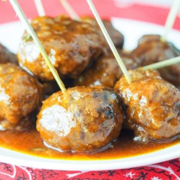 close up view of bbq meatballs on white plate sitting on red bandana