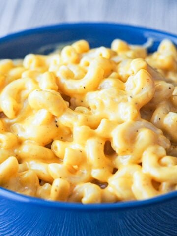 close-up view of mac and cheese in a blue bowl sitting on a white wooden tabletop