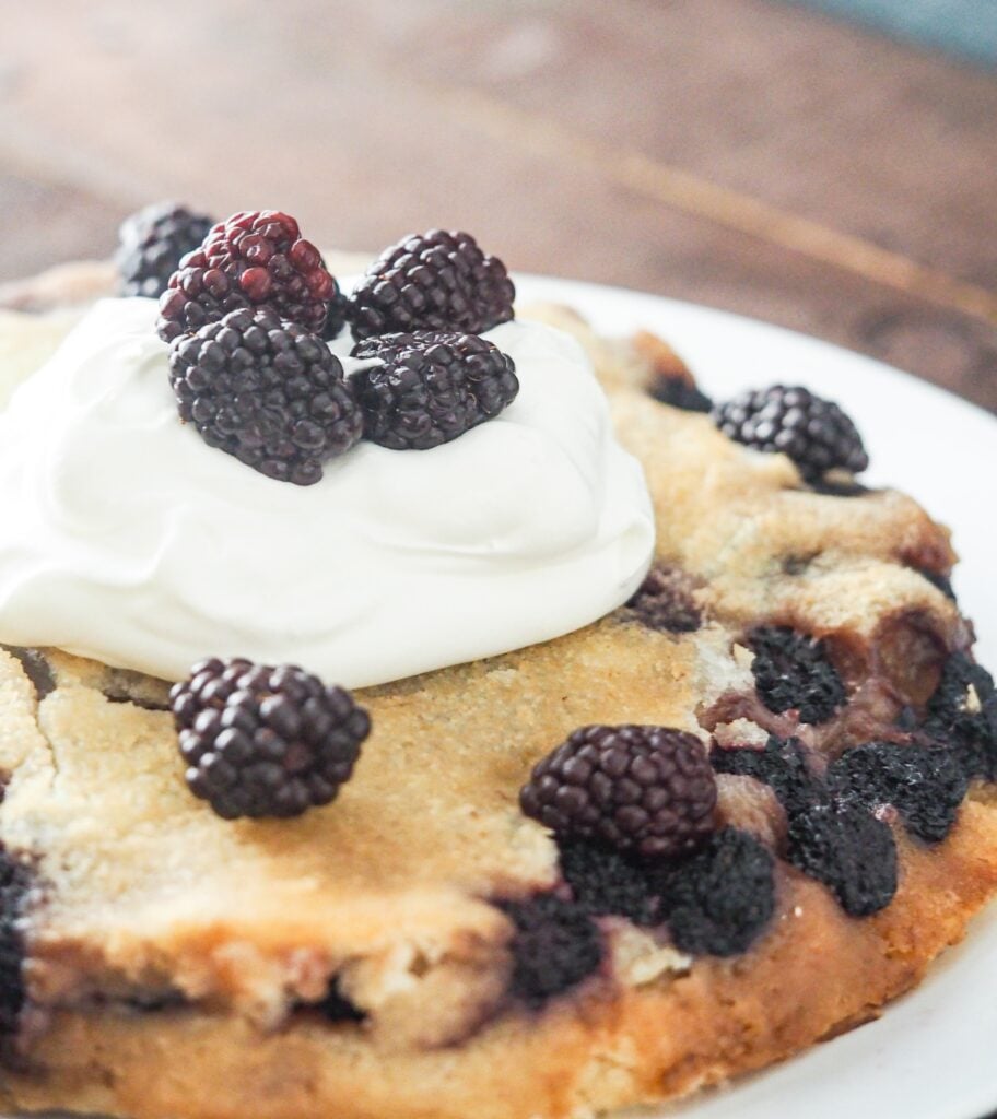 Close-up view of blackberry cobbler from the side with whipped topping and fresh berries