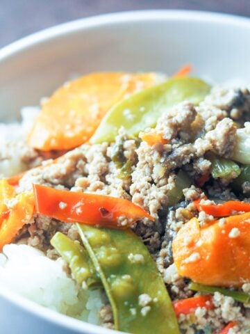 close up of ground pork stir fry with vegetables on top of jasmine rice in white bowl