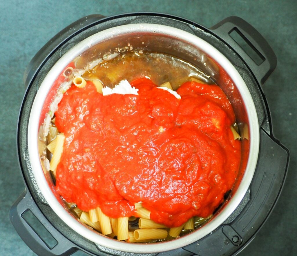 overhead view of ziti ingredients in instant pot topped with spaghetti sauce
