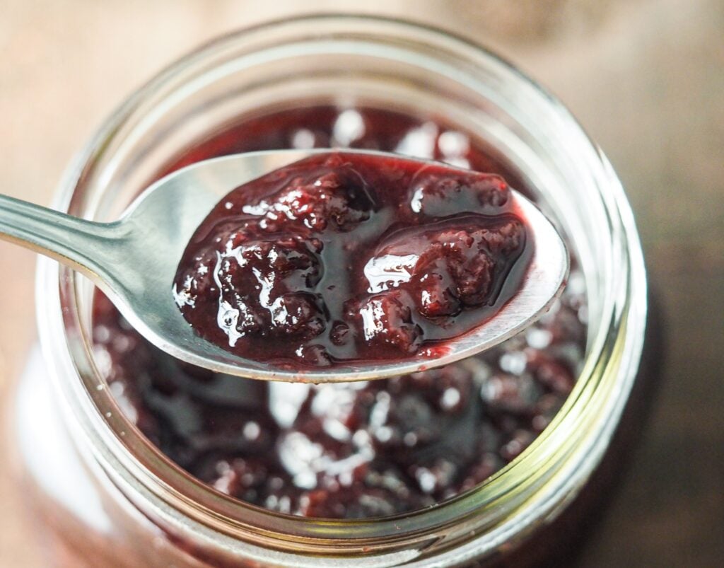 overhead shot of cherry jam in a canning jar with a spoonful suspended above the jar
