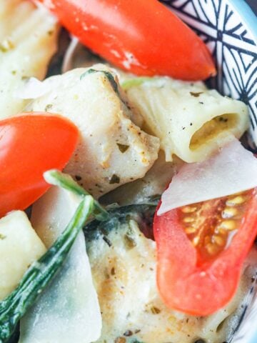 close up view of pesto chicken pasta in bowl with fresh tomato