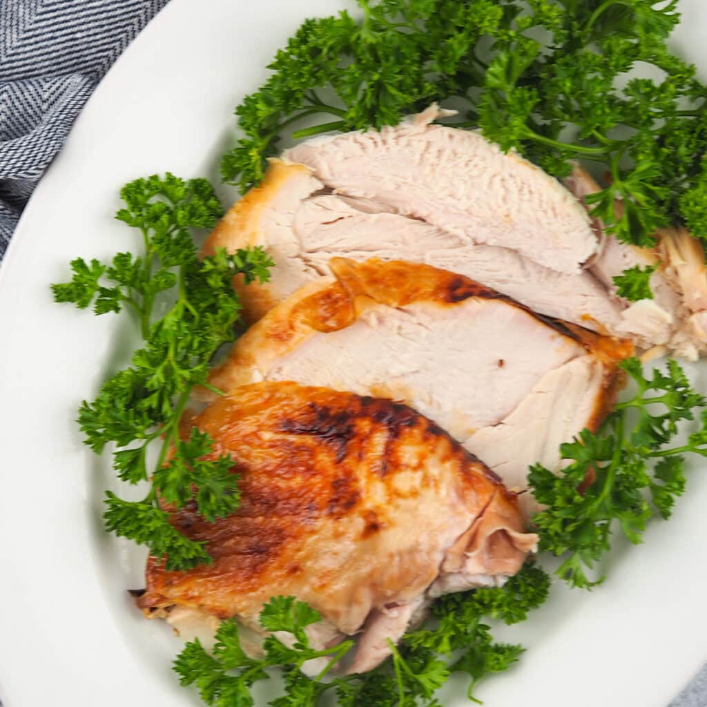 sliced turkey breast on white platter with parsley