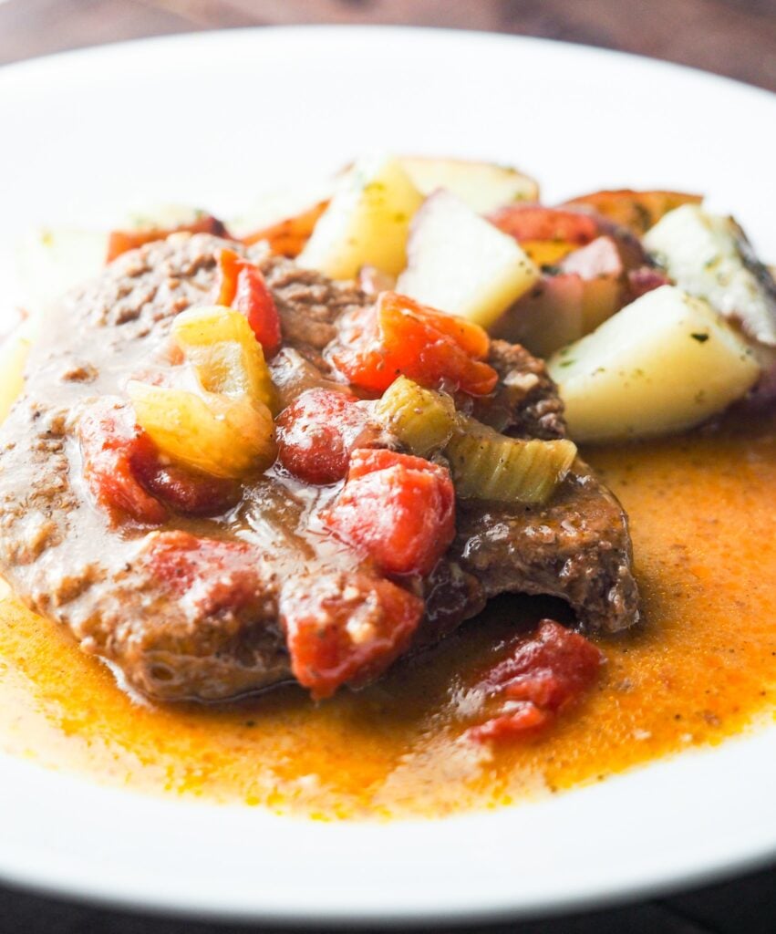 swiss steak with tomatoes on white plate with parslied potatoes