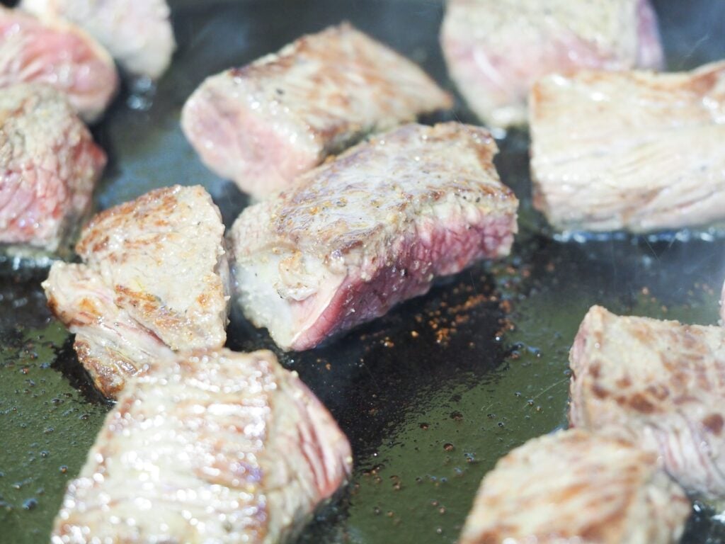close up view of cubed beef browning in a cast iron pan