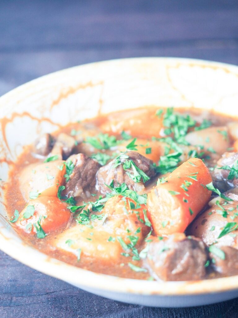 beef stew sprinkled with parsley in cream bowl with fall leaf detail