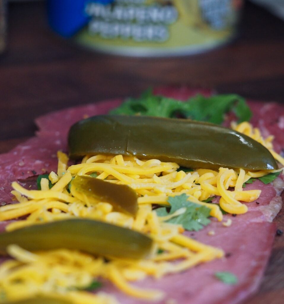 seasoned thin cut beef with herbs, cheddar cheese, and sliced pickled jalapenos on a wooden cutting board